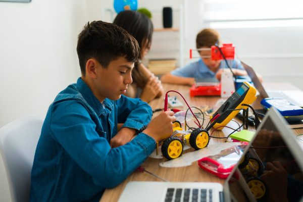 Latin teen boy using building a robot prototype Group of junior high teens doing a technology project and learning how to build robots in their electronics class